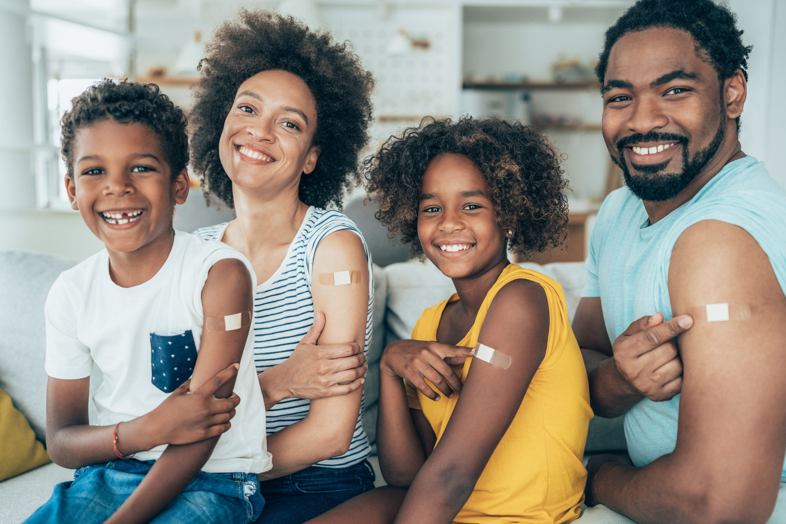  Portrait of a Black family, smiling and displaying the band-aids on their arms, after getting a vaccination.